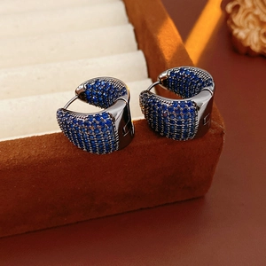 Macro detail of gunmetal huggie earrings with pave set blue zircons on red velvet