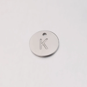 Detailed macro view of silver mirror-finish stainless steel round pendant with letter K