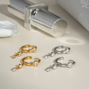 Detail of gold and silver hoop earrings with diamond drop chains on neutral background