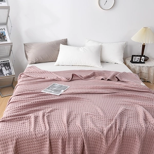 Cozy pink waffle cotton blanket draped on a bed within a minimalist bedroom setting