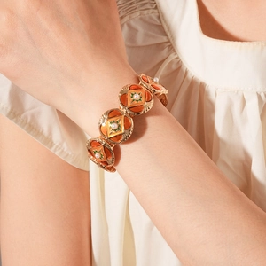 Close-up of vintage gold bangle with orange enamel and pearls on a model's wrist