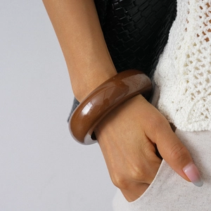 Chic dark brown resin bangle on wrist paired with a stylish textured bag and knitwear