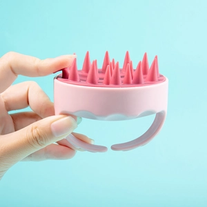 Detail of pink silicone scalp massager brush showing soft bristles on blue background