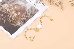 Détail d'un bracelet chaîne doré orné d'une perle blanche et d'un pendentif cœur lisse