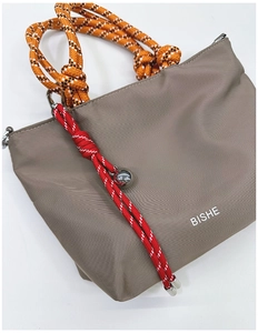 Detail of khaki nylon handbag with orange braided rope handle and silver metal ball