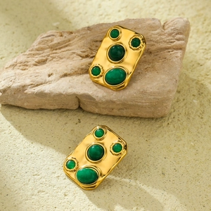 Detail view of gold vintage earrings with green stones on natural stone prop