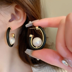 Detailed close-up of a C-shaped gold hoop earring featuring black leather and a large pearl