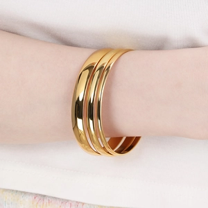 Close-up of three stacked polished gold titanium bracelets on a female model wrist