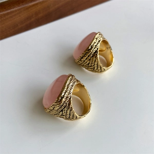 Detailed view of two gold textured rings with large oval pink stones on white surface