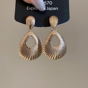 Close-up of golden teardrop earrings with radial texture and hollow design details