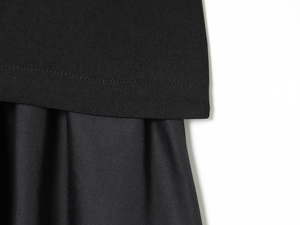 Detailed macro view of black dress showing double-needle hem and pleated fabric texture