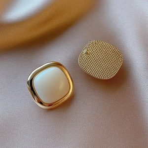 Detail of cream acrylic square stud earrings with golden textured metal back on silk