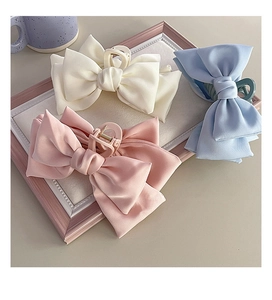 Close-up of three large satin bow hair claws in white, pink, and light blue on a tray