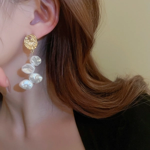 Elegant gold baroque pearl drop earrings featuring pleated geometric metal discs on a model