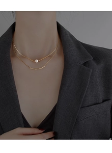 Detail of baroque pearl pendant on a double-layer golden necklace shown on model