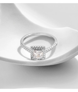 Macro shot of silver square cut diamond ring on a white decorative petal texture