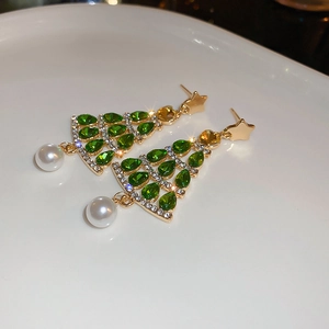 Close-up of gold Christmas tree earrings with green crystals and pearl drop on ceramic