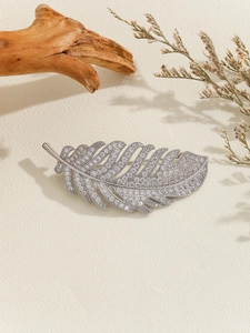 Detailed macro view of a silver feather brooch with sparkling cubic zirconia on wood