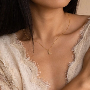 Elegant gold letter L pendant necklace with crystals worn by a model in lace attire