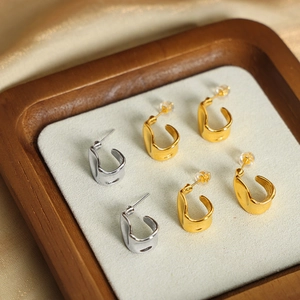 Minimalist geometric U-shaped earrings in gold and silver finish on a wooden display tray
