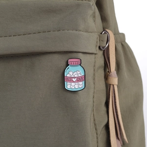 Close-up of a blue Take Care medicine bottle enamel pin on an olive green canvas bag