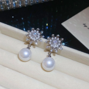 Detailed close-up of elegant snowflake pearl earrings with cubic zirconia in a jewelry box