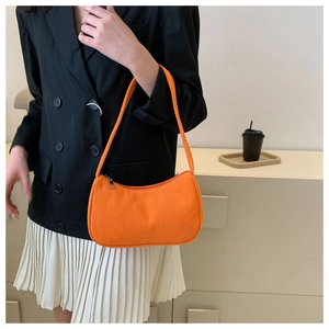 Close-up of the orange corduroy baguette bag worn over the shoulder by a model