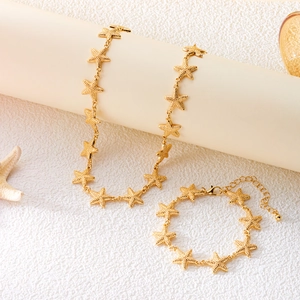 Detailed close-up of golden starfish-shaped necklace and bracelet set on a beach prop