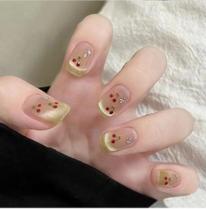 Détail de manucure aux cerises avec dégradé œil de chat doré et strass délicats