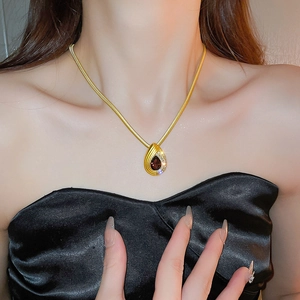 Detail view of gold snake chain necklace with water drop pendant and dark red gemstone