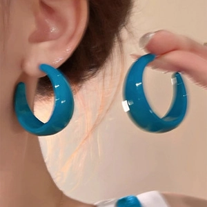 Detail of light blue C-shaped thick hoop earrings with a glossy resin finish on ears