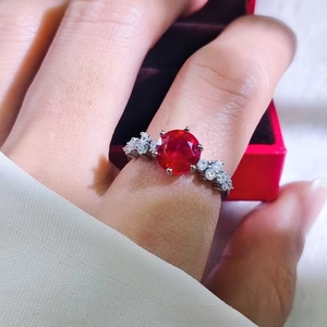 Close-up of a 2-carat red ruby ring with side diamonds on a silver band shown on a finger