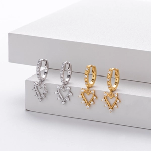 Detail of silver and gold heart-shaped earrings with micro-set zircons on white steps