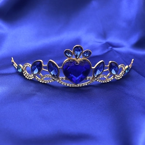 Detailed shot of golden crown featuring large blue heart crystal on blue silk fabric