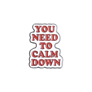 Detail of metal pin with red lettering 'YOU NEED TO CALM DOWN' on white enamel