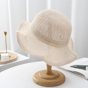 Detailed knit texture of beige sun hat with hollow pattern and wavy brim on wood stand
