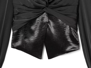 Close-up of a black V-neck shirt featuring a twist knot waist and mixed fabric details