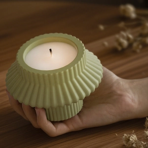 Close-up of a sage green textured ceramic candle holder held by hand in home setting