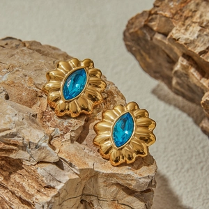 Detailed close-up of retro gold petal earrings with blue marquise stone on a rock