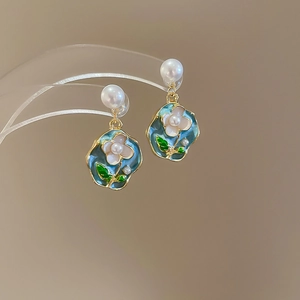 Detail of blue enamel earrings with white flower charms and pearl studs in gold finish