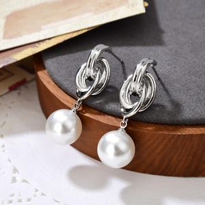 Elegante verschlungene Creolen in Silber mit weißen Perlen auf grauem Samtuntergrund