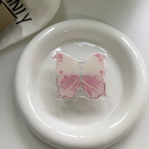 Detail shot of a pink butterfly phone griptok made of clear acrylic on a ceramic dish