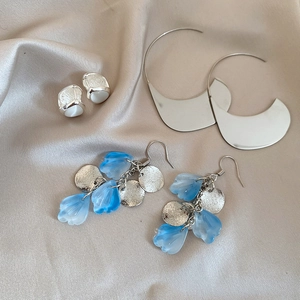 Macro shot of acrylic petal tassel earrings and silver crescent hoops on champagne silk