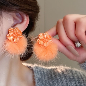 Close-up of orange resin flower stud and fluffy pompom earring on female model ear