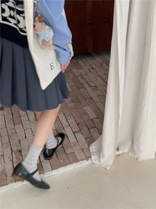 Detail shot of light grey striped mid-calf socks styled with Mary Jane shoes and pleated skirt