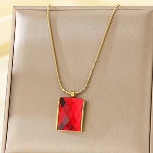Detail of red square crystal pendant on golden snake chain necklace over a jewelry stand