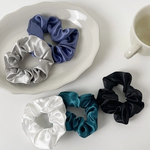 Close-up of five satin silk scrunchies in blue, silver, white, green, and black colors