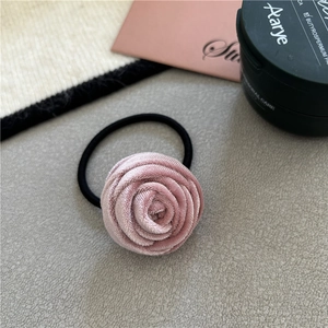 Close-up of a pink velvet rose hair tie showing soft petal texture and elastic band