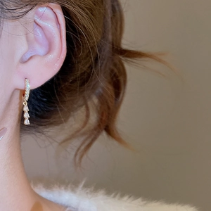 Macro side view of gold drop earrings with zircon crystals on a model's ear