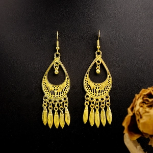 Detail of ethnic golden peacock earrings featuring leaf tassels on a black texture background